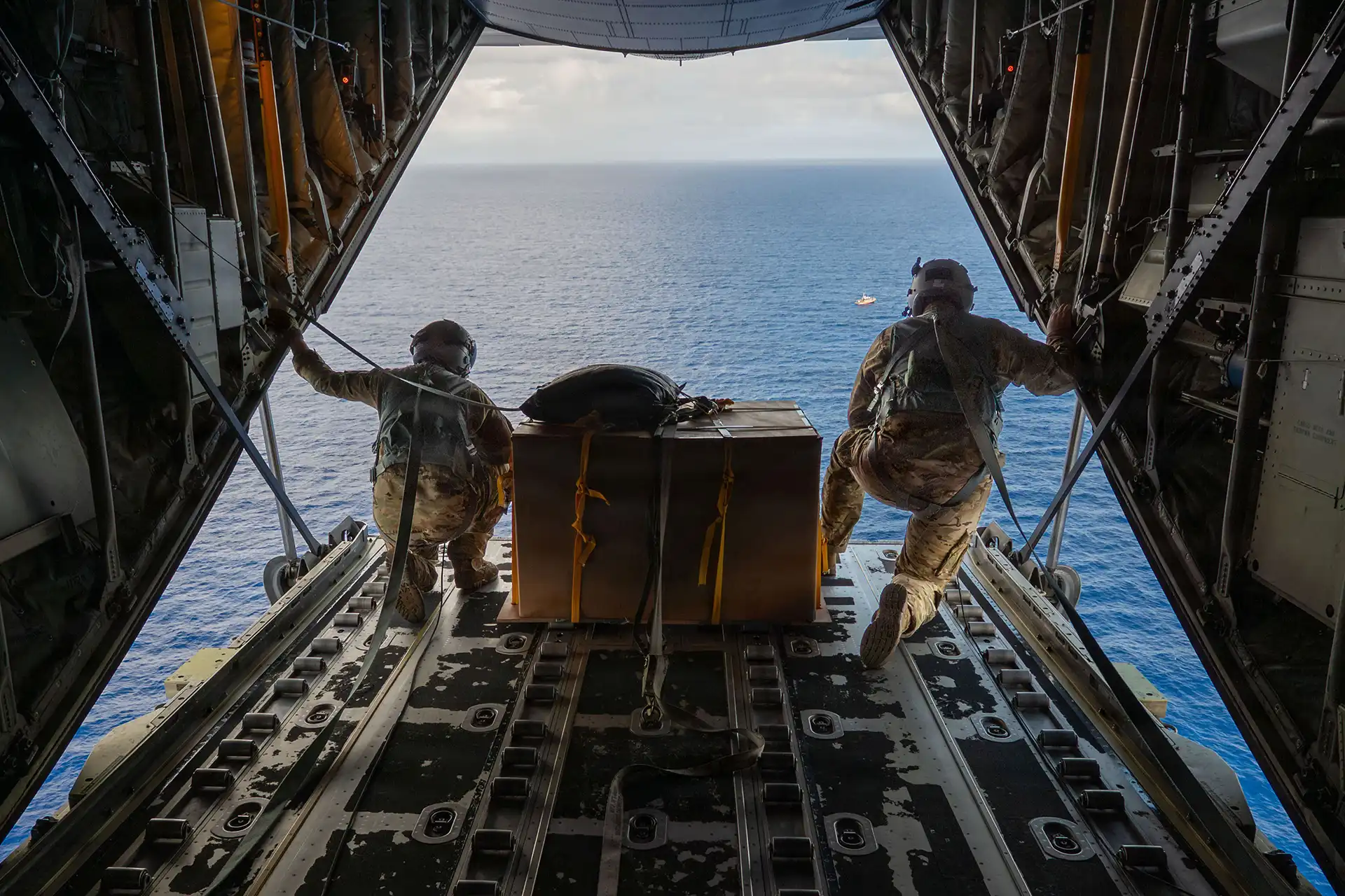 Loadmasters releasing a cargo bundle from a C-130 ramp over the sea